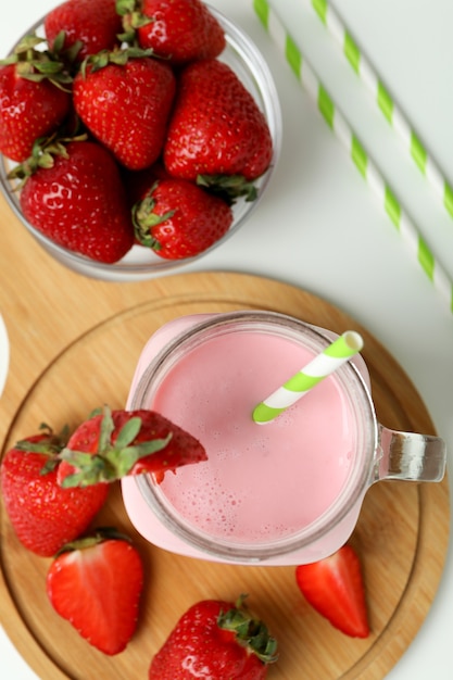 Pot en verre de milk-shake aux fraises et ingrédients sur fond blanc