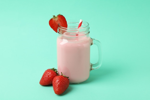 Pot en verre de milk-shake aux fraises et ingrédients sur fond de menthe