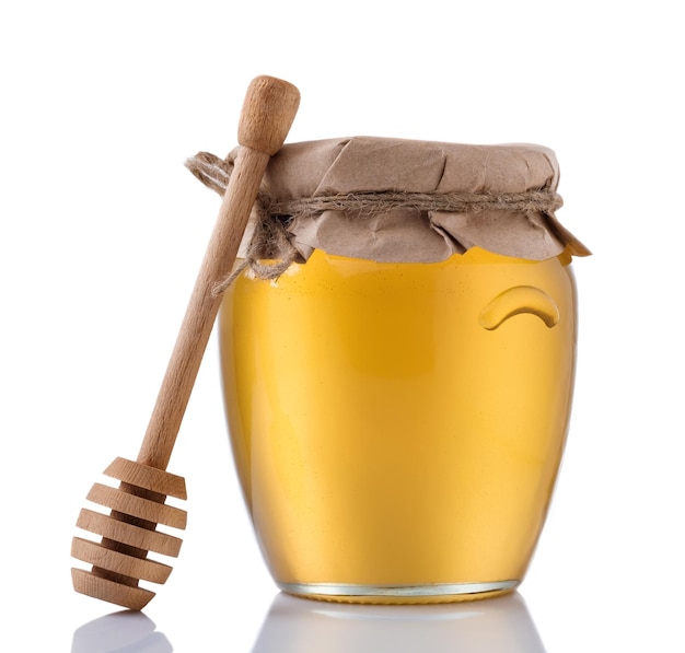 Pot en verre plein de miel et bâton en bois sur fond blanc