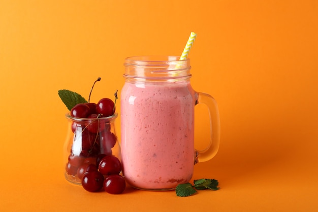 Pot en verre de smoothie aux cerises et ingrédients sur fond orange