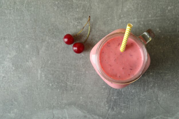 Pot en verre de smoothie aux cerises et d'ingrédients sur une table texturée grise