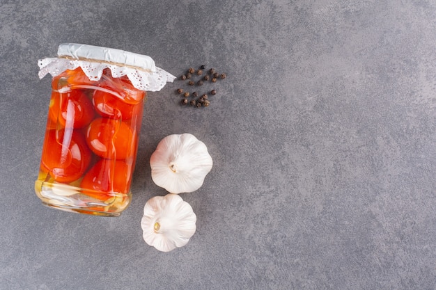 Pot en verre de tomates marinées et d'ail sur table en pierre.