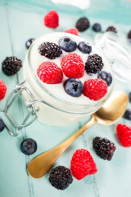 Un pot de yogourt avec des bleuets, des mûres et des framboises sur un plateau en bois