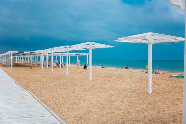 Des poteaux de bois blancs sur la plage de sable pour les parapluies et les auvents Des gens qui se baignent et se reposent par une journée ensoleillée
