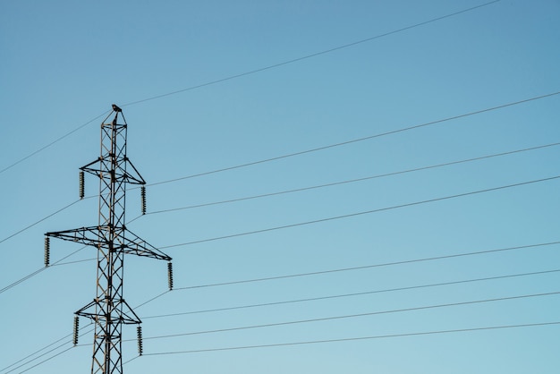 Poteaux avec des fils de haute tension sur un ciel bleu au soleil.