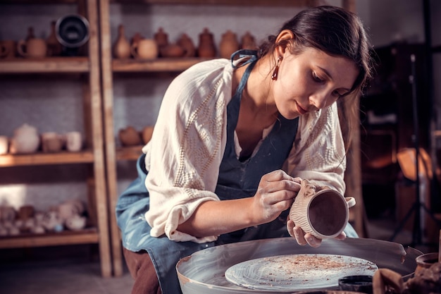 Poterie élégante femme moulant un vase d'argile sur un tour de potier. Confection de plats en céramique.