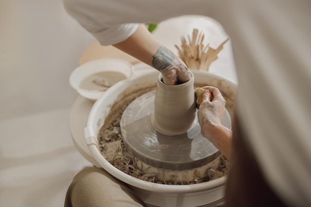 Poterie féminine en tablier donnant forme à un vase d'argile sur un outil de poterie filant dans un atelier de céramique