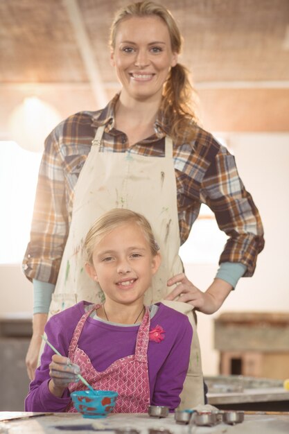 Potier féminin aidant la fille à peindre à l'atelier de poterie