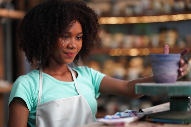 Photo potier à la main de jeune fille afro faisant un vase d'argile dans un atelier de poterie, propriétaire d'entreprise.