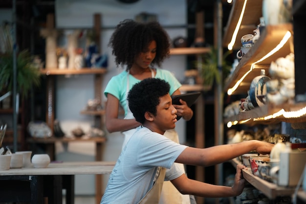 Potier à la main de jeune fille Afro faisant un vase d'argile dans un atelier de poterie, propriétaire d'entreprise.