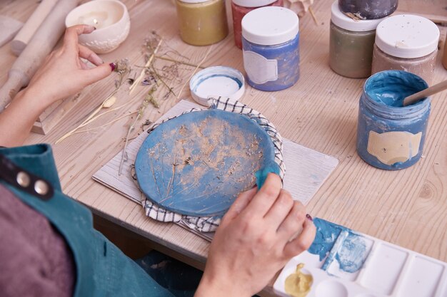 Un potier professionnel travaille sur des assiettes de peinture dans l'atelier Une femme céramiste peint une assiette de couleur bleue