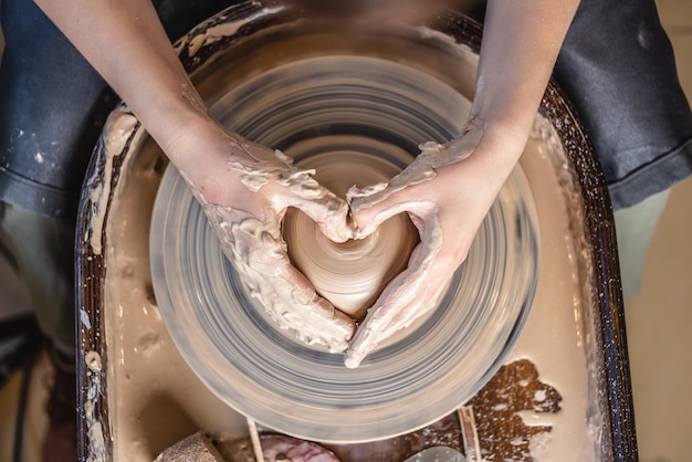 Un potier travaille avec de l'argile sur une roue de potier dans l'atelier. Les mains des femmes montrent un signe de coeur