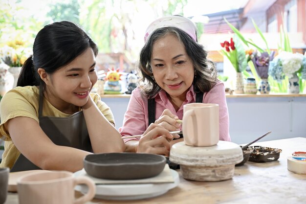 Potière asiatique âgée apprenant à une jeune femme à colorier sur la tasse en céramique