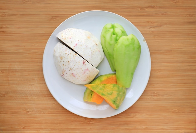 Potiron japonais, chao et chayote tranchés dans un plateau en plastique sur fond de planche de bois.