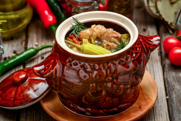 Des pots en argile avec des pommes de terre au four et de la viande de poulet avec de la citrouille et des légumes verts hachés sur une planche en bois