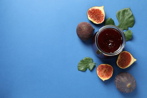 Pots avec confiture de figues et ingrédients sur fond bleu