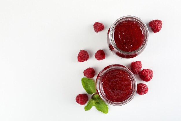 Pots de confiture de framboises avec des ingrédients sur fond blanc