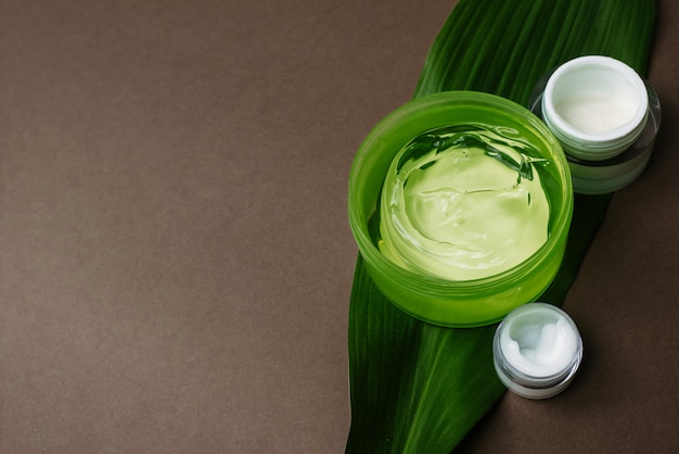 Pots de crème blanche hydratante et de gel d'aloès vert sur une feuille de palmier.