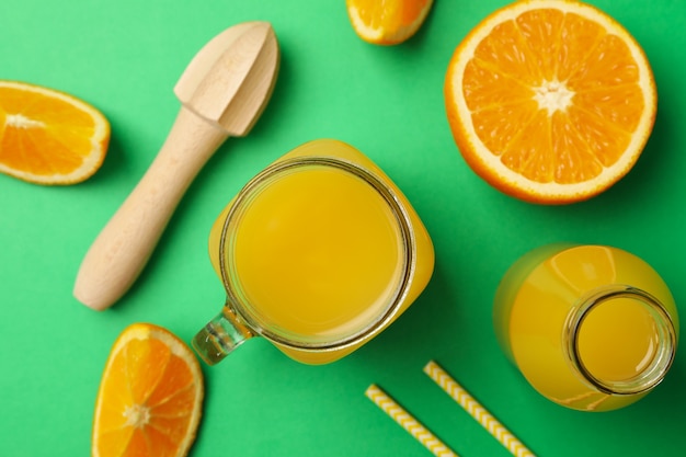 Pots de jus d'orange, tranches d'orange, presse-agrumes et pailles sur vert