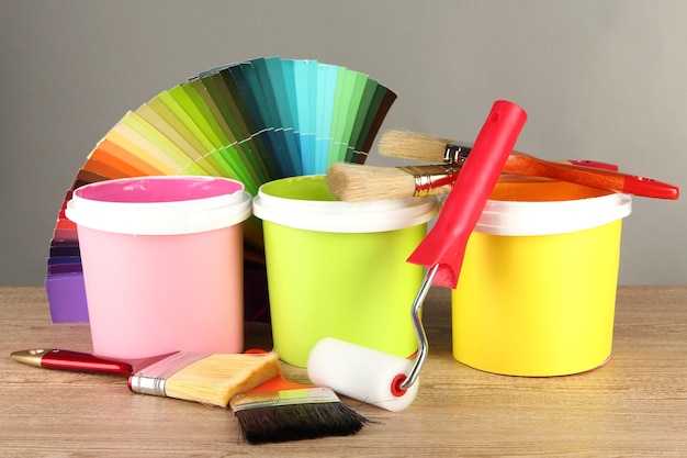 Pots de peinture pinceaux et échantillons de couleur sur table en bois sur fond gris