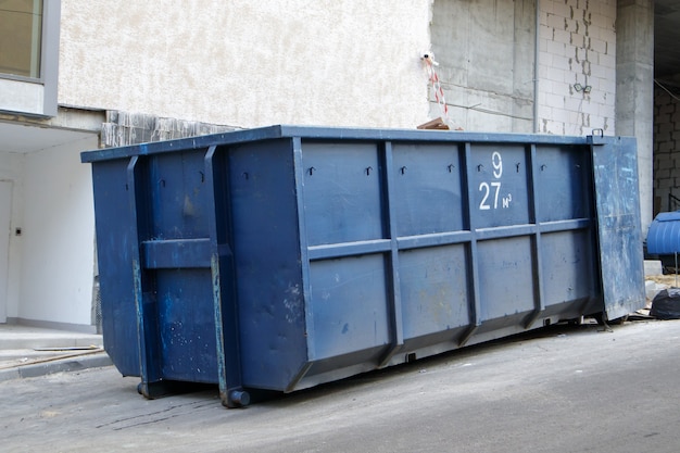 Photo poubelle industrielle bleue durable en métal pour les déchets extérieurs sur le chantier de construction. grande corbeille pour déchets ménagers ou industriels. un tas de déchets.