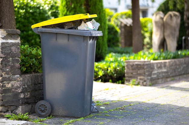 Une poubelle pleine de déchets se tient sur le trottoir à côté de la rue en attente d'être ramassée et vidée.