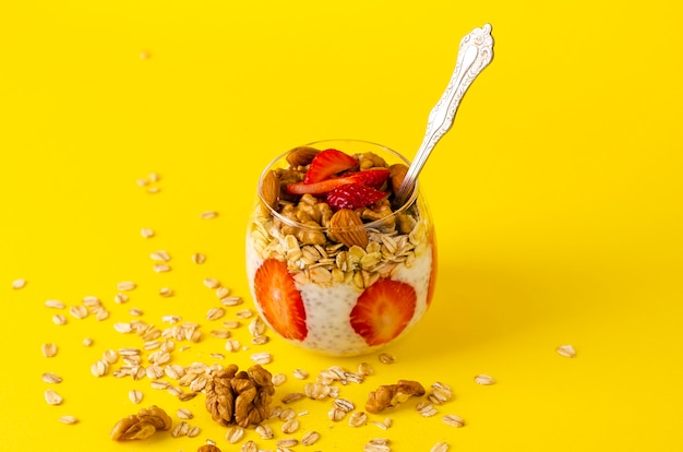 Pouding au yaourt chia avec fraises, flocons d’avoine et noix dans un verre jaune