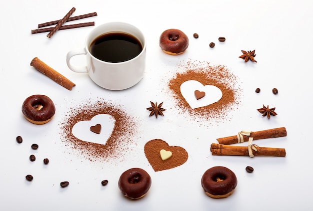 Poudre de cacao en forme de coeur, bâtonnets de menthe et une tasse d'espresso avec des beignets au chocolat.