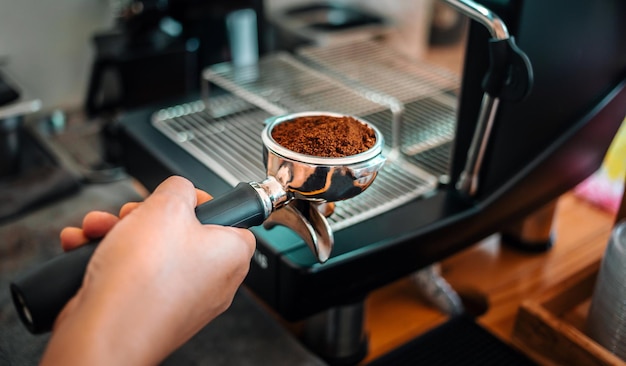 Poudre de café moulu dans un porte-filtre faisant un café expresso dans la main du barista