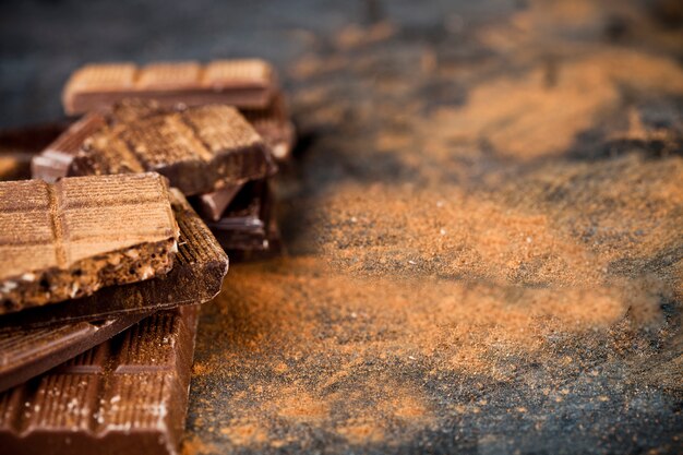 Poudre de cannelle et de chocolat cassé, empilée sur fond noir.