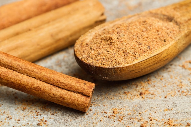 Poudre de cannelle sur une cuillère en bois et des bâtons sur une table