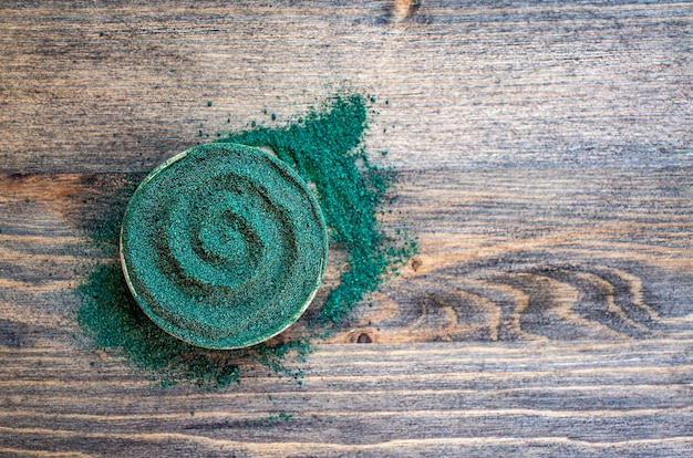 Poudre de chlorelle ou de spiruline en forme de spirale sur un fond en bois foncé avec un espace de copie