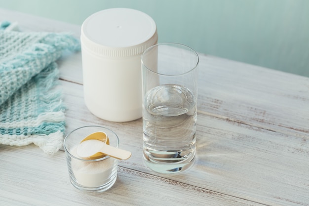 Poudre de collagène dans un bol, verre d'eau et mesure cuillère sur un fond bleu clair. Apport supplémentaire de protéines. Concept de supplément de beauté et de santé naturelle.