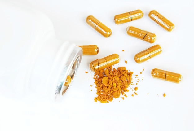 Poudre de curcuma et capsules sur fond blanc