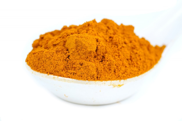 Poudre de curcuma en cuillère blanche.