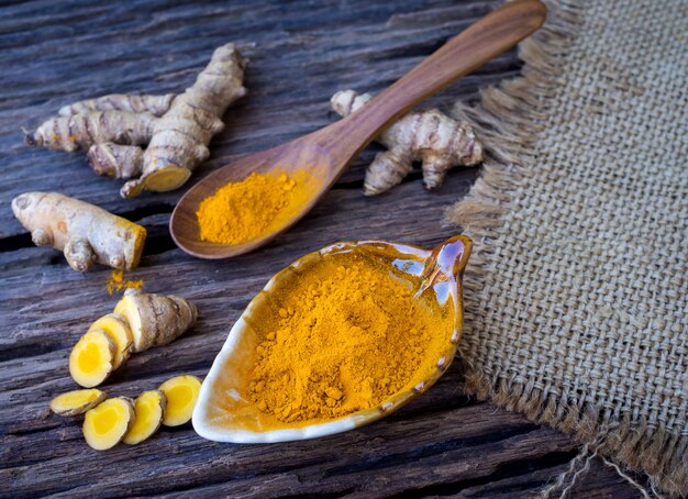 Poudre de curcuma et curcuma frais en cuillère avec feuille verte sur une vieille table en bois. Herbal