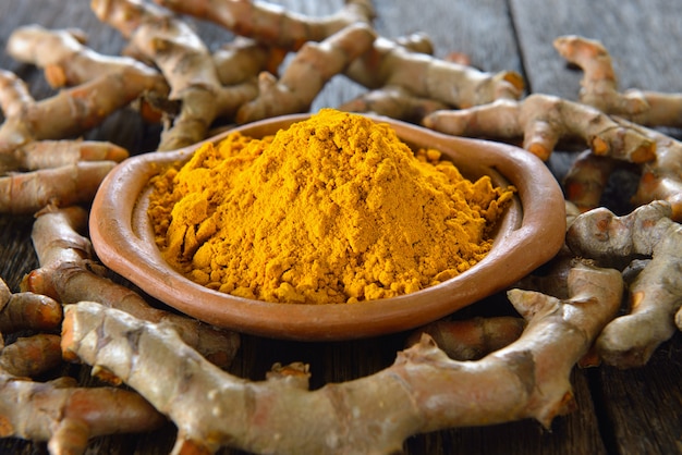 Poudre de curcuma et curcuma sur une surface en bois