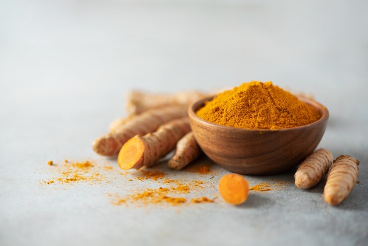 Photo poudre de curcuma dans un bol en bois et racine de curcuma frais sur fond de béton gris. bannière avec espace de copie