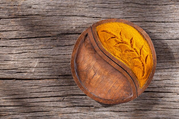 Poudre de curcuma dans un bol sur fond de bois