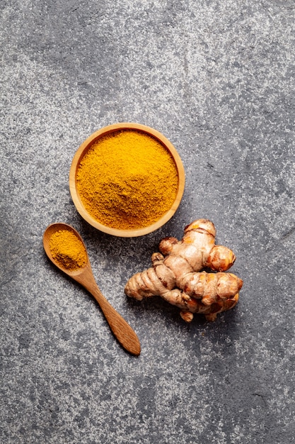 Poudre de curcuma et racine de curcuma frais sur béton gris.