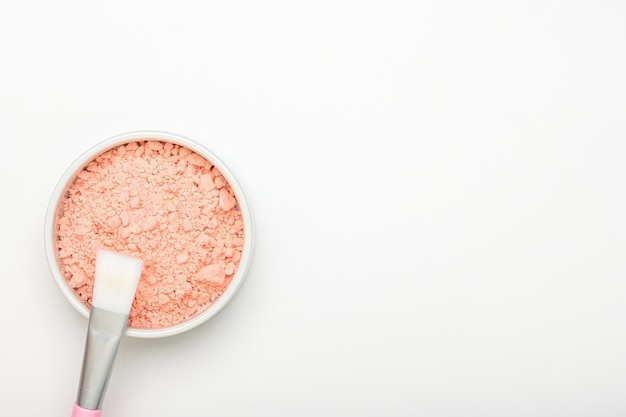 Poudre de masque d'alginate rose dans un bol avec un pinceau sur la vue de dessus de fond blanc. Masque visage liftant nettoyant au collagène et aux acides. Texture argile, poudre sèche. Produit de soin de beauté nettoyant cosmétique.