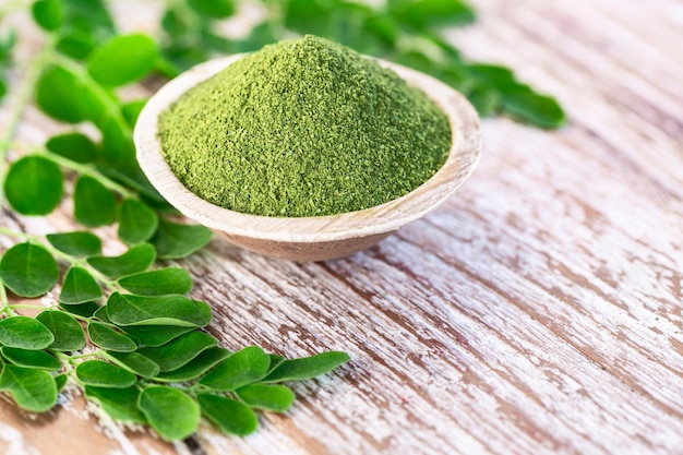 Poudre de Moringa dans un bol en noix de coco avec des feuilles de Moringa fraîches originales sur fond en bois