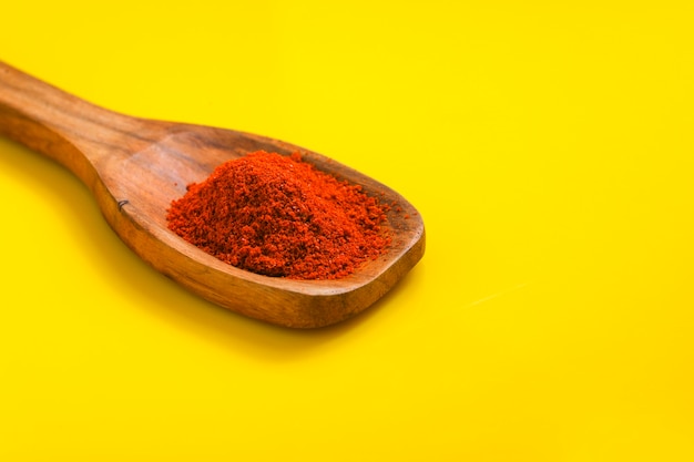 Poudre de piment dans une cuillère en bois avec froid rouge sec sur une surface jaune