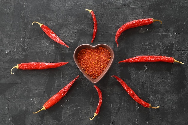 Photo poudre de piments rouges chauds dans un bol en forme de coeur sur une table en pierre noire concept d'amour vue de dessus