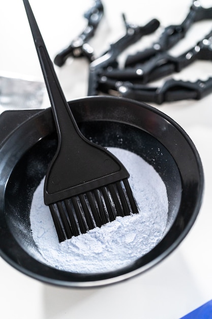 Poudre de teinture de couleur de cheveux dans un bol à mélanger en plastique noir sur fond blanc.