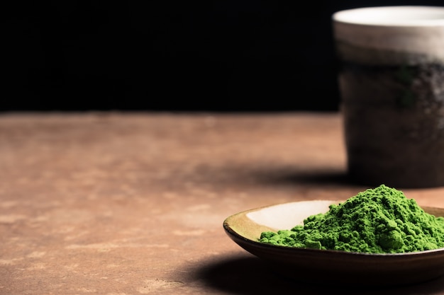 Poudre De Thé Vert Avec Une Tasse En Céramique Sur La Table, Fond Noir. Espace Libre Pour Le Texte