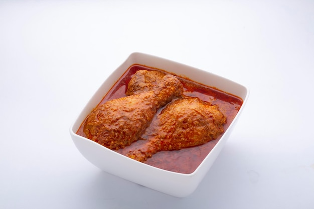 Poulet au curry ou masala, poulet au curry de style Kerala utilisant de la noix de coco frite de manière traditionnelle et disposé dans un récipient en céramique blanche placé sur fond blanc.