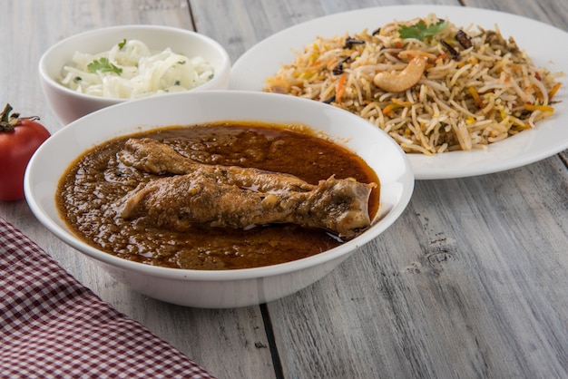 Photo poulet au curry ou masala rougeâtre populaire, avec un morceau de cuisse proéminent, servi dans un bol avec du riz pilaf, du chapati ou du roti et de la salade
