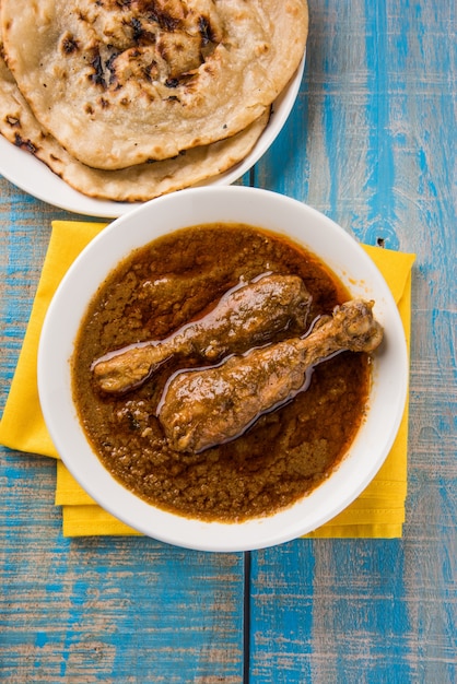 Photo poulet au curry ou masala rougeâtre populaire, avec un morceau de cuisse proéminent, servi dans un bol avec du riz pilaf, du chapati ou du roti et de la salade