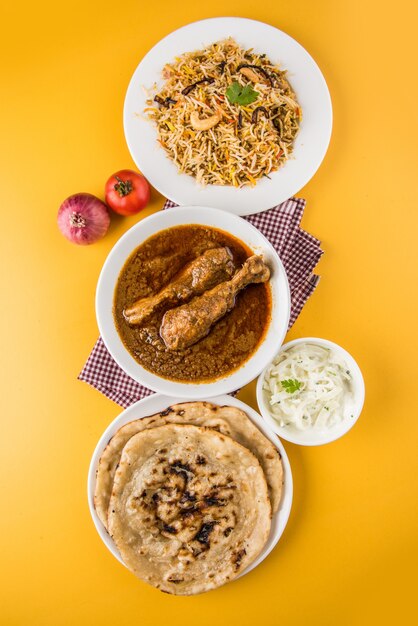 Poulet au curry ou masala rougeâtre populaire, avec un morceau de cuisse proéminent, servi dans un bol avec du riz pilaf, du chapati ou du roti et de la salade